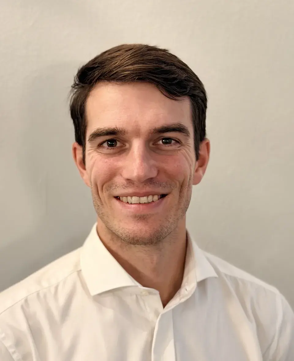 Erik Bräunel, Chair of the Board, with short dark hair and a white shirt, smiling in front of a light-coloured wall