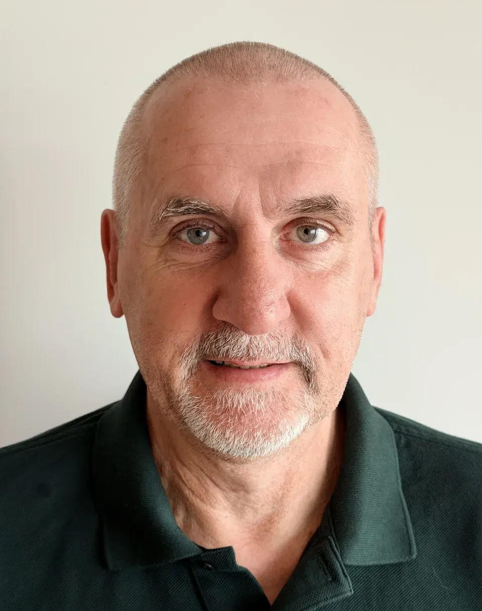 Dr. Ralf Schaub, board member, with a grey beard and a dark green polo shirt, in front of a light-coloured wall